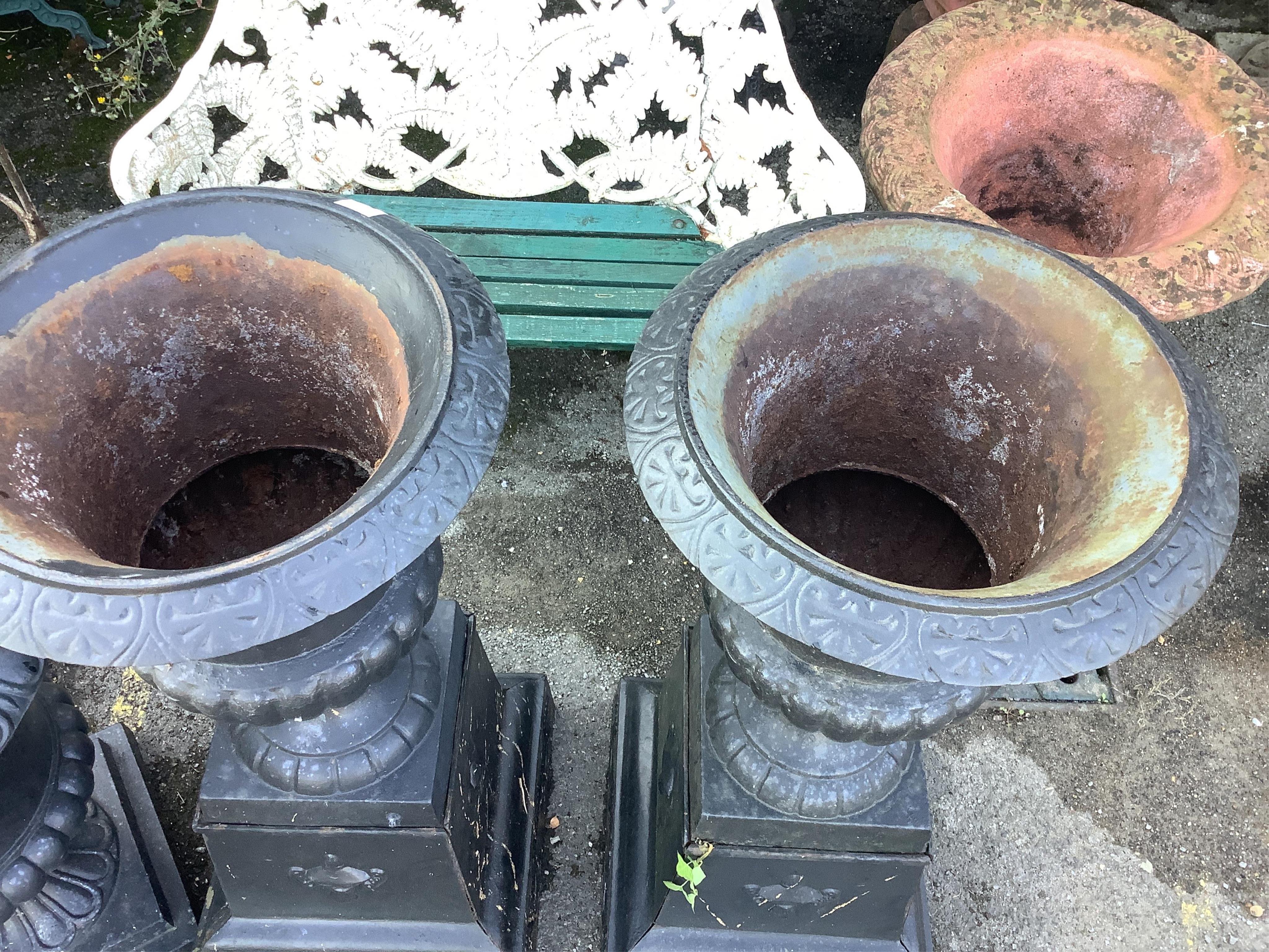 A pair of Victorian style black painted cast iron campana shaped garden urns, on square plinths, diameter 50cm, height 113cm. Condition - fair